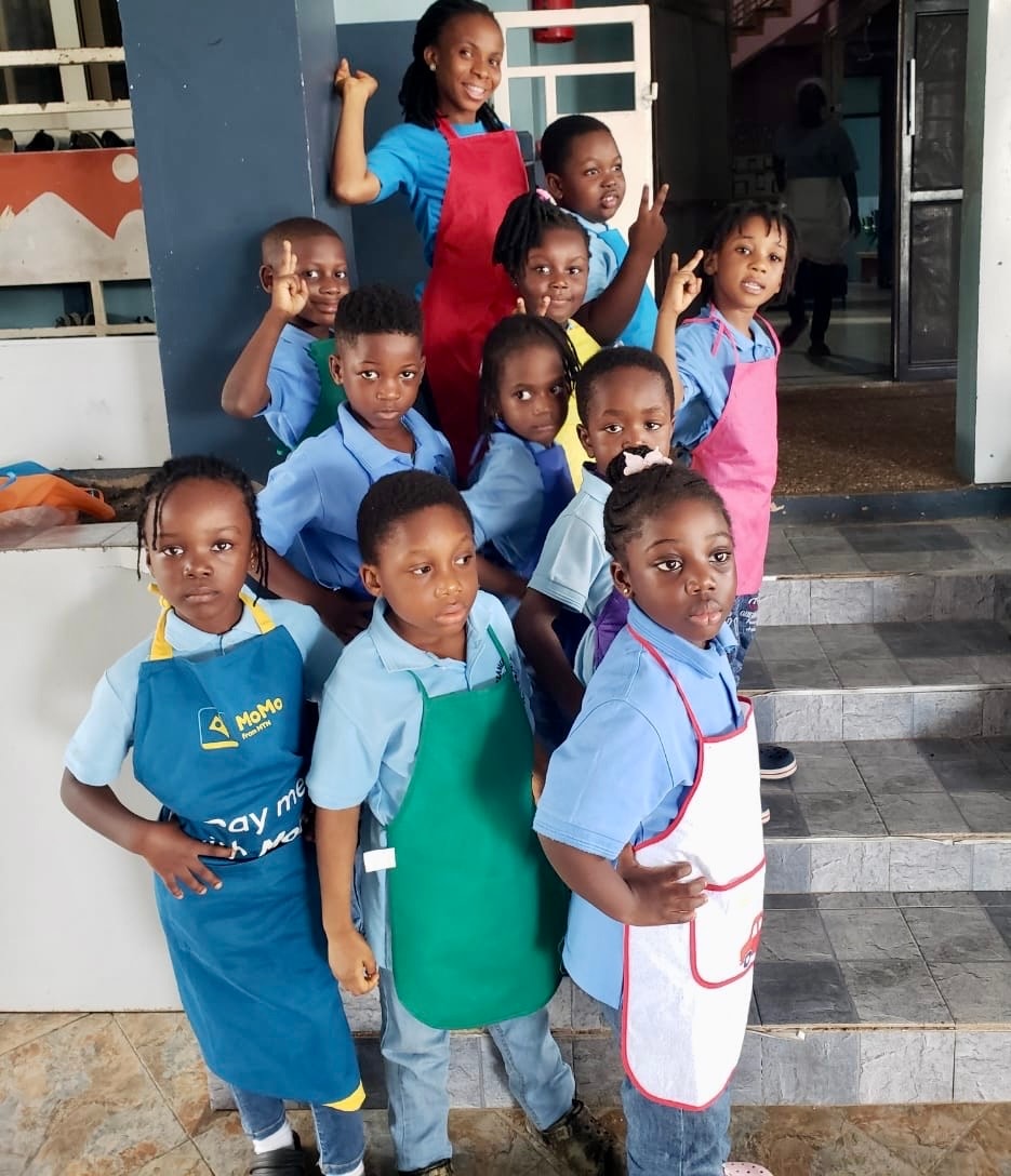 Teacher and students in colourful aprons posing together outside the school
