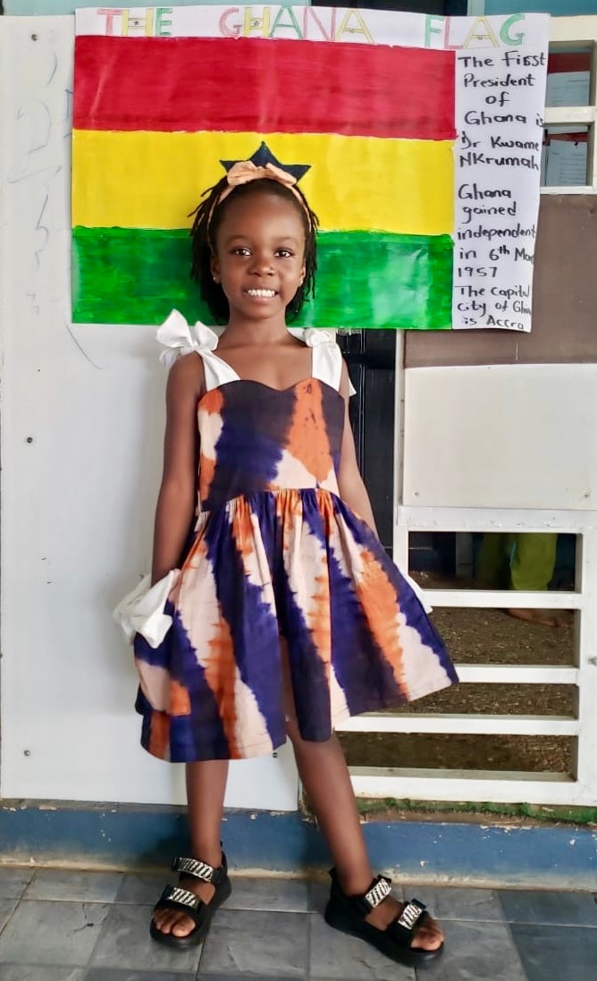 Girl in tie-dye dress smiling in front of the Ghana flag