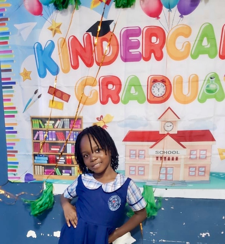 Smiling girl graduate posing in front of the Kindergarten Graduate banner